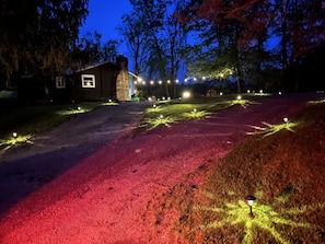 A house with a stone chimney, a paved driveway, and a lawn with string lights. - Bean’s Place - Adorable ridge top cabin five miles from Ohio University! (Athens)