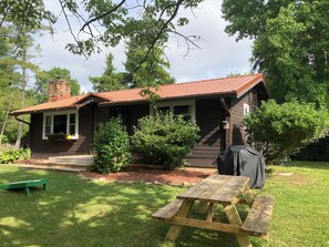 Eine Holzhütte mit Metalldach, umgeben von Bäumen und einem Picknicktisch.