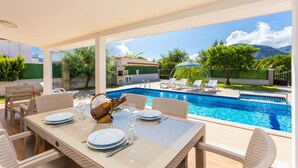An outdoor pool area with a table set for dining, surrounded by lounge chairs and a view of a mountainous landscape. - Villa Vista - Four Bedroom Villa, Sleeps 8 (Dalyan)