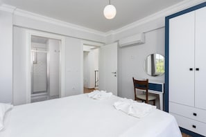 Ein Schlafzimmer mit einem großen Bett, einem Schreibtisch mit Stuhl, einem Kleiderschrank und einer Klimaanlage.