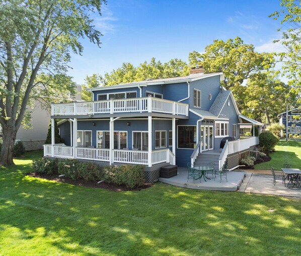 A two-story house with a balcony, a patio with outdoor furniture, and a well-maintained lawn.