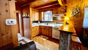 Un interior de cabaña con paredes de madera, una cocina con estufa y una zona de comedor.