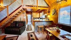 Interior acogedor de una cabaña con escalera de madera, comedor y cocina.