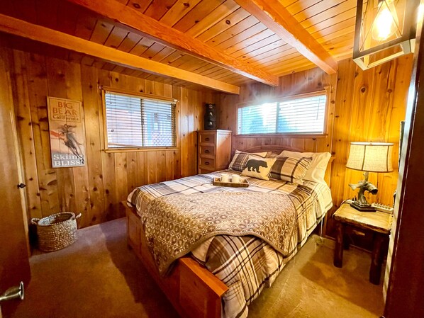 A cozy wooden cabin bedroom with a bed, dresser, and nightstand.
