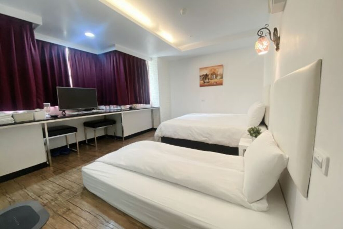 Habitación de hotel con escritorio, dos camas, televisión y una pequeña mesa con una planta.