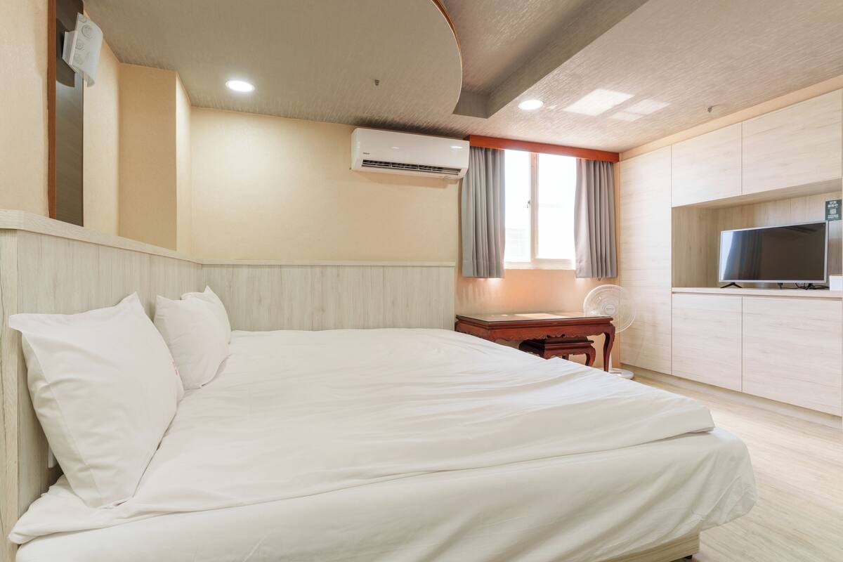 Ein Hotelzimmer mit Bett, Schreibtisch, Fernseher und Klimaanlage.
