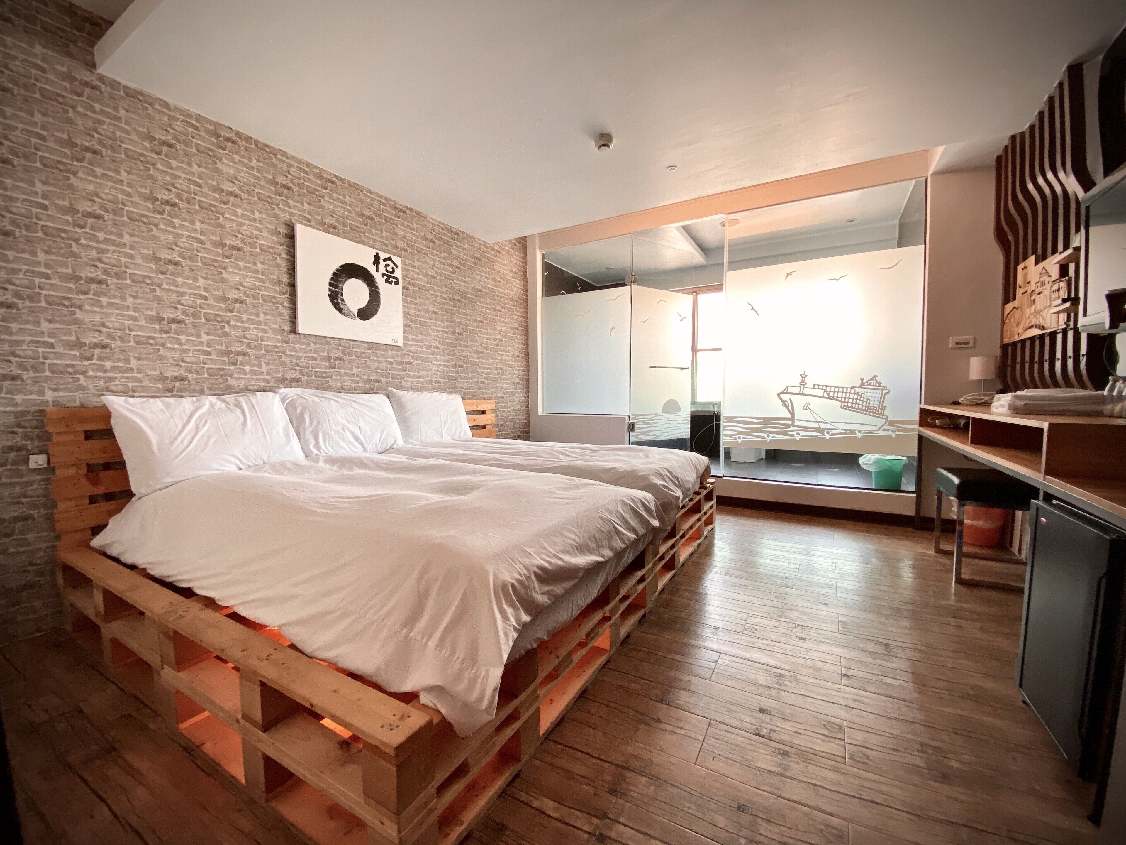 A bedroom with a wooden bed, a brick wall, and a large mirror reflecting a ship and seagulls.