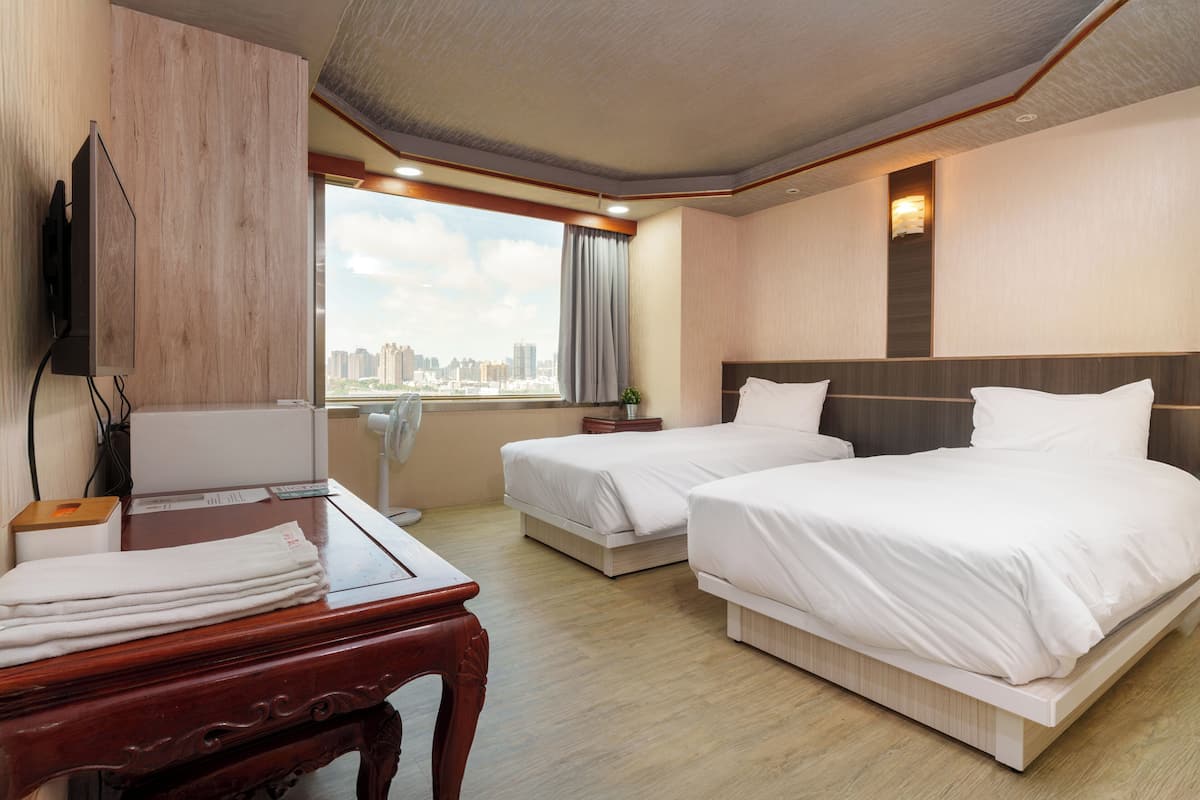 Ein Hotelzimmer mit zwei Betten, einem Schreibtisch, einem Fernseher und Blick auf die Stadt.
