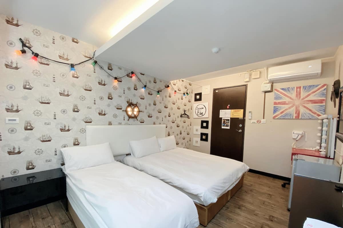 Ein Hotelzimmer mit zwei Betten, maritime Wandtapete, einer Wandleuchte im Schiffsdesign, einer Tür mit Union Jack und einem Schminktisch mit Spiegel.