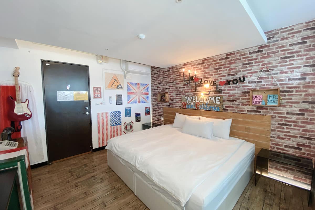 Ein Schlafzimmer mit Backsteinwand, einem Bett mit weißer Bettwäsche, einer Gitarre und verschiedenen Wanddekorationen, darunter Flaggen und Schilder.