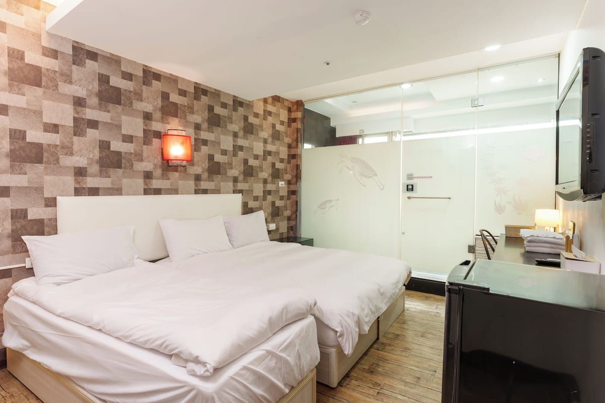 Ein modernes Hotelzimmer mit einem großen Bett, einer Duschkabine aus Glas und einem Flachbildfernseher.