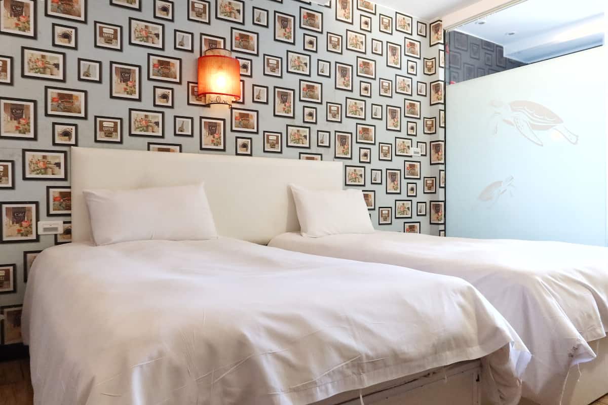 Ein Doppelbett mit weißen Leinen in einem Zimmer mit gemustertem Wandpapier und einer Wandlampe.