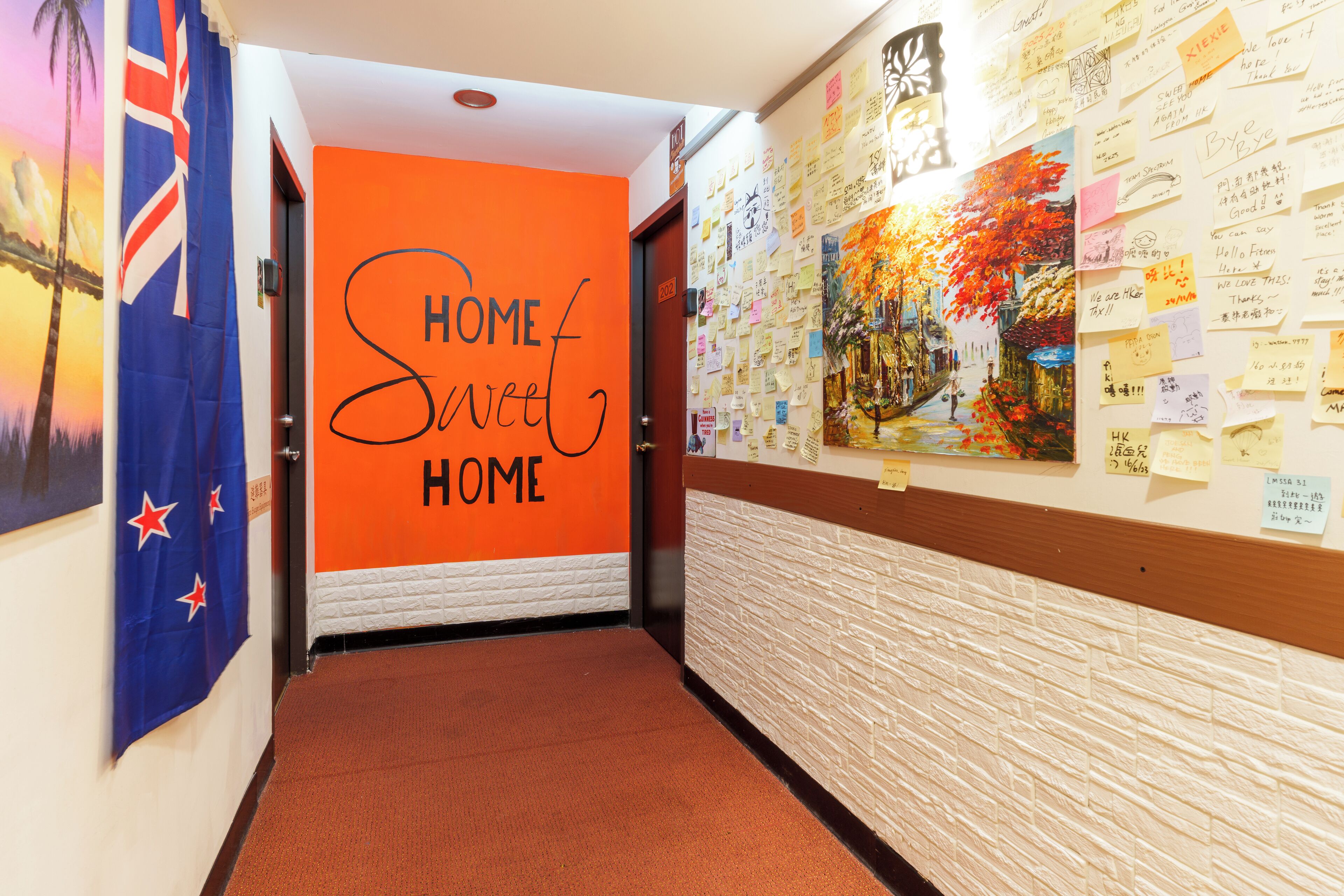 A hallway with an orange wall displaying 'HOME Sweet HOME' and a wall covered with various notes and drawings.