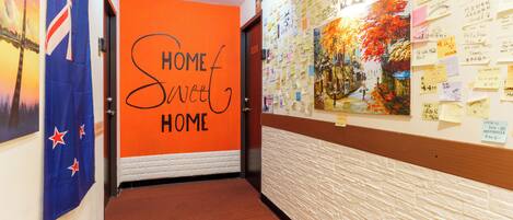 A hallway with an orange wall displaying 'HOME Sweet HOME' and a wall covered with various notes and drawings.
