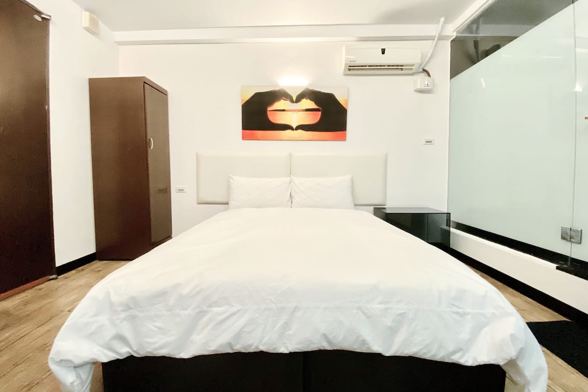 Ein Hotelzimmer mit einem großen Bett, einem Kleiderschrank, einem Nachttisch und einer Wand-Klimaanlage.