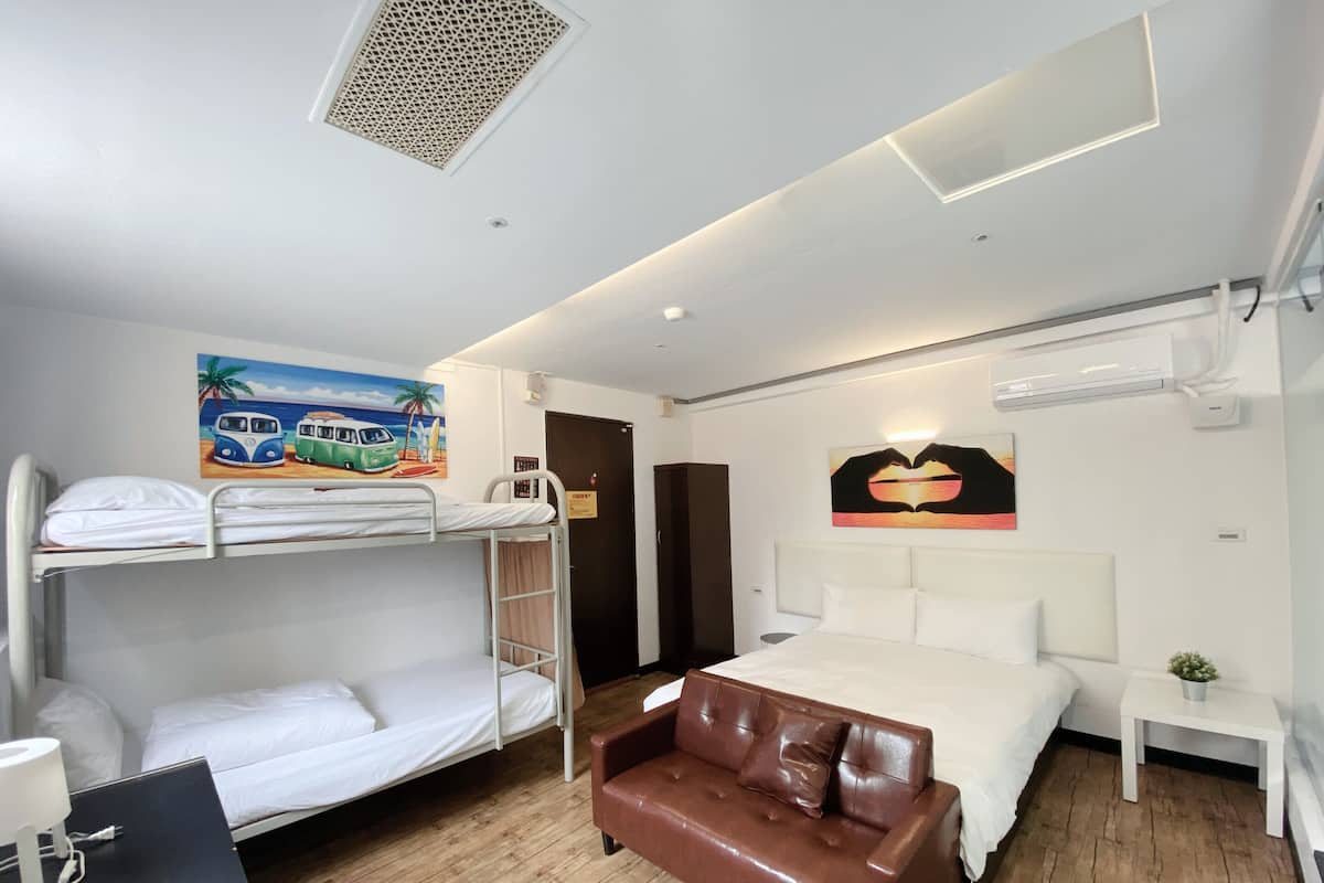Ein Hotelzimmer mit Etagenbetten, einem Einzelbett, einem braunen Ledersofa, einem kleinen Tisch mit Pflanze und einem Bild von Oldtimern an der Wand.