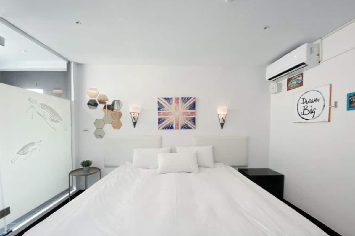 Ein modernes Schlafzimmer mit einem großen Bett, einer wandmontierten Klimaanlage und Wanddekoration, darunter eine Union Jack Flagge und ein Schild mit der Aufschrift 'Dream Big'.