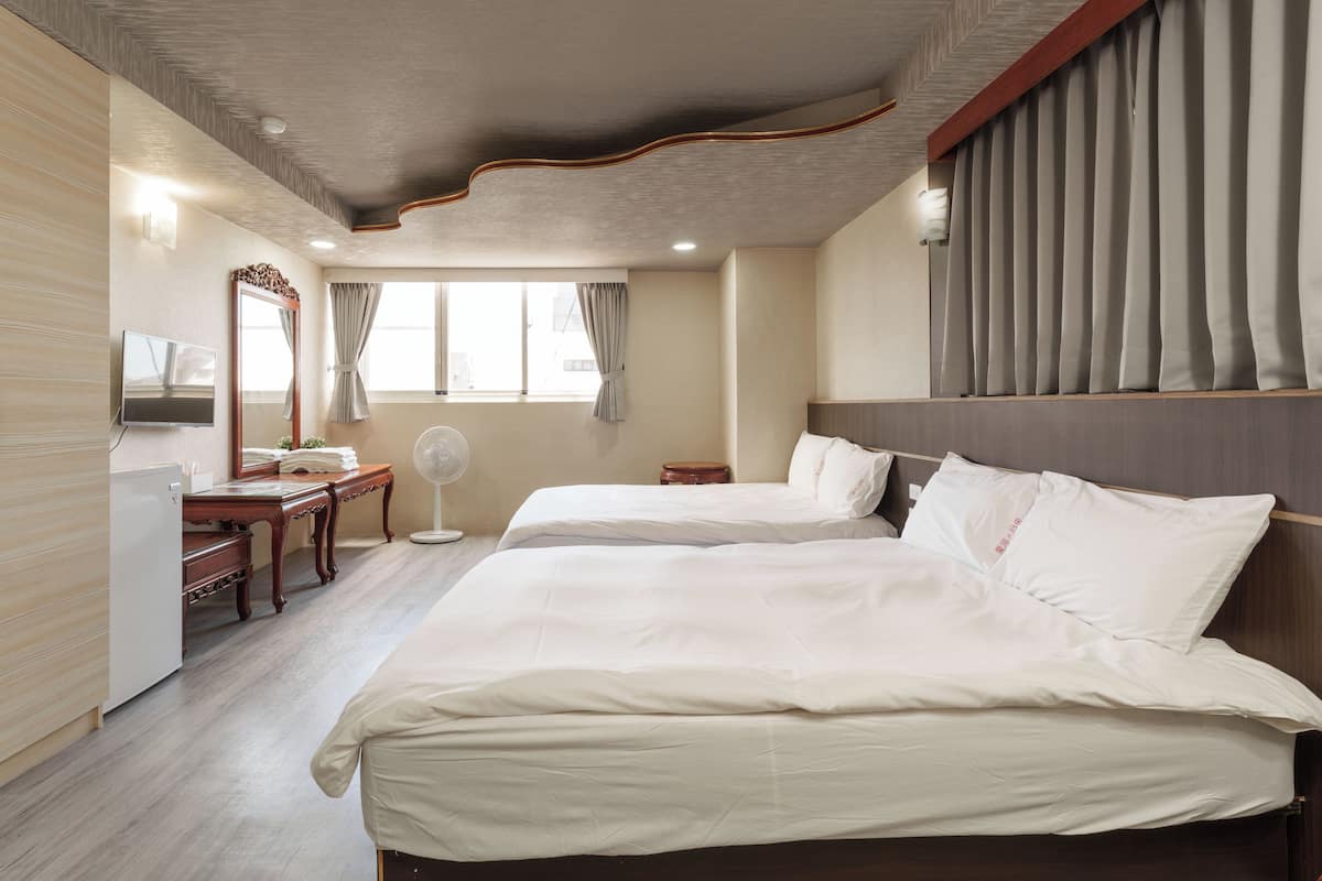 Ein Hotelzimmer mit zwei Betten, einem Schreibtisch, einem Spiegel und einem Fernseher.