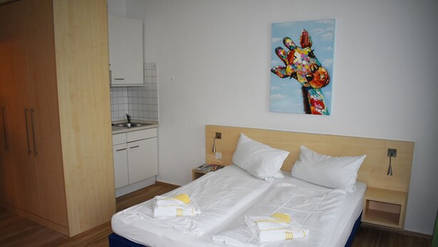A hotel room with a large bed, a small kitchenette, and a painting on the wall. - Posthus Apartment 103, close to the beach and central (Borkum)