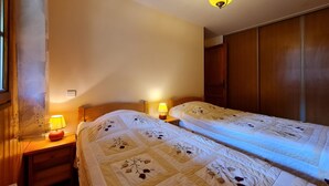 A bedroom with two beds, wooden headboards, bedside lamps, and a wardrobe. - Chalet Genépi - Apartment 1 (Le Grand-Bornand)