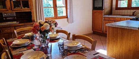 A dining area with a table set for six, wooden cabinets, a kitchen with an oven, and a window with curtains.