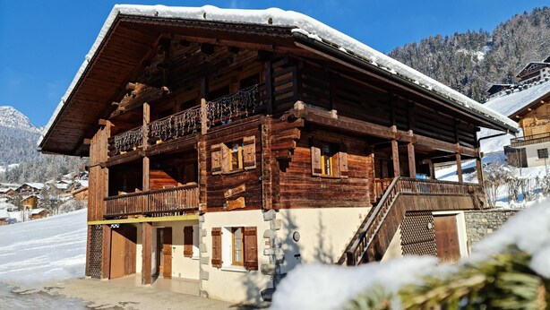 A wooden chalet with a balcony, stone foundation, and a staircase leading to the upper floor. - Chalet Genépi - Apartment 1 (Le Grand-Bornand)