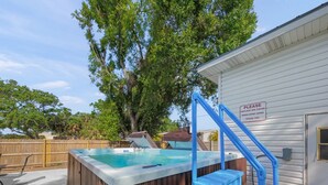 Una vasca idromassaggio in un giardino privato con un patio in legno e una casa bianca.