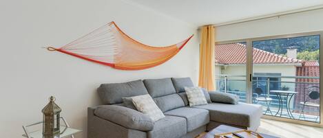 A modern living room with a grey sectional sofa, a glass coffee table, and a hammock.