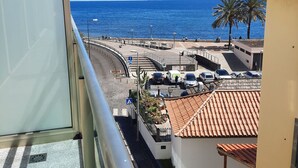 A balcony with a view of the sea, a parking area, and a building with a tiled roof. - Sunny Beach Machico Apartment (Machico)