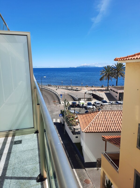 Un balcon avec vue sur la mer, un espace de stationnement et un bâtiment doté d’un toit en tuiles.