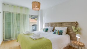A bedroom with a large bed, a green bedspread, a wooden headboard, and a hanging light fixture. - Sunny Beach Machico Apartment (Machico)