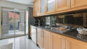 A modern kitchen with wooden cabinets, a granite countertop, and a sliding glass door leading to a balcony. - Sunny Beach Machico Apartment (Machico)
