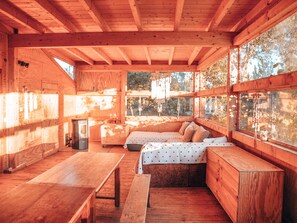 Ein Holzblockbau-Innenraum mit Essbereich, einer Sitzbank und großen Fenstern mit Blick ins Freie.