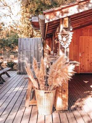 Eine Holzterrasse mit einem Korbwicker-Korb voll Pampasgras, einer Holzbank und einem rustikalen Holzgebäude mit Tür und Fenstern.