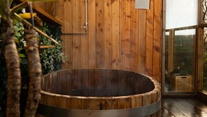A wooden spa tub in a room with wooden walls and a large window. - Spacious sea-view apt. w/ hot tub & sauna overlooking St Ives Bay (Hayle)