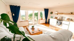 A cozy living room with a sofa, a wooden coffee table, and large green plants. - Spacious sea-view apt. w/ hot tub & sauna overlooking St Ives Bay (Hayle)
