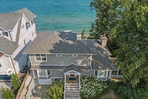 A two-story house with a front porch, a small front yard, and a view of the ocean.