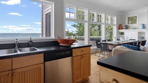 Une cuisine moderne dotée d’une grande fenêtre donnant sur la mer, de meubles en bois et d’un plan de travail noir.