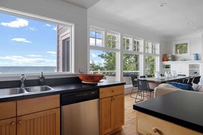 Een moderne keuken met een groot raam dat uitkijkt over de zee, houten kastjes en een zwart aanrecht.