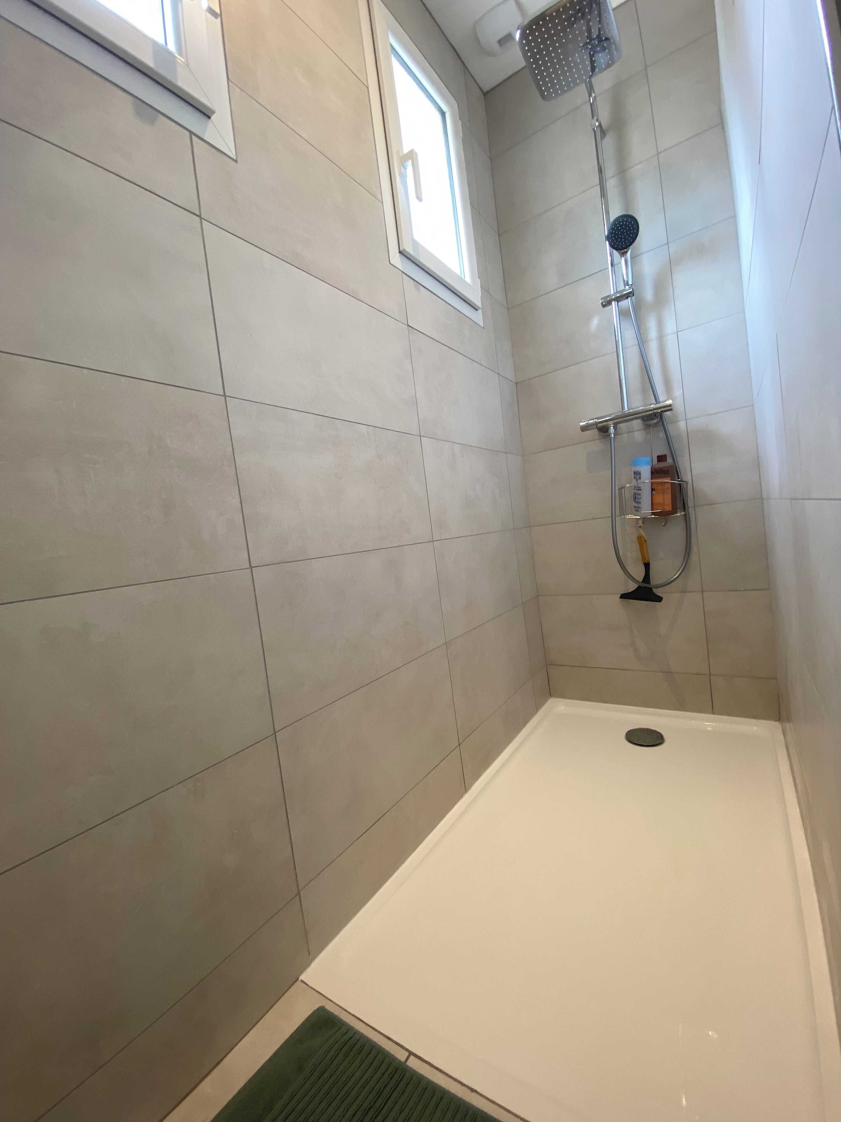Een kleine, moderne badkamer met een douche, toilet en een raam.