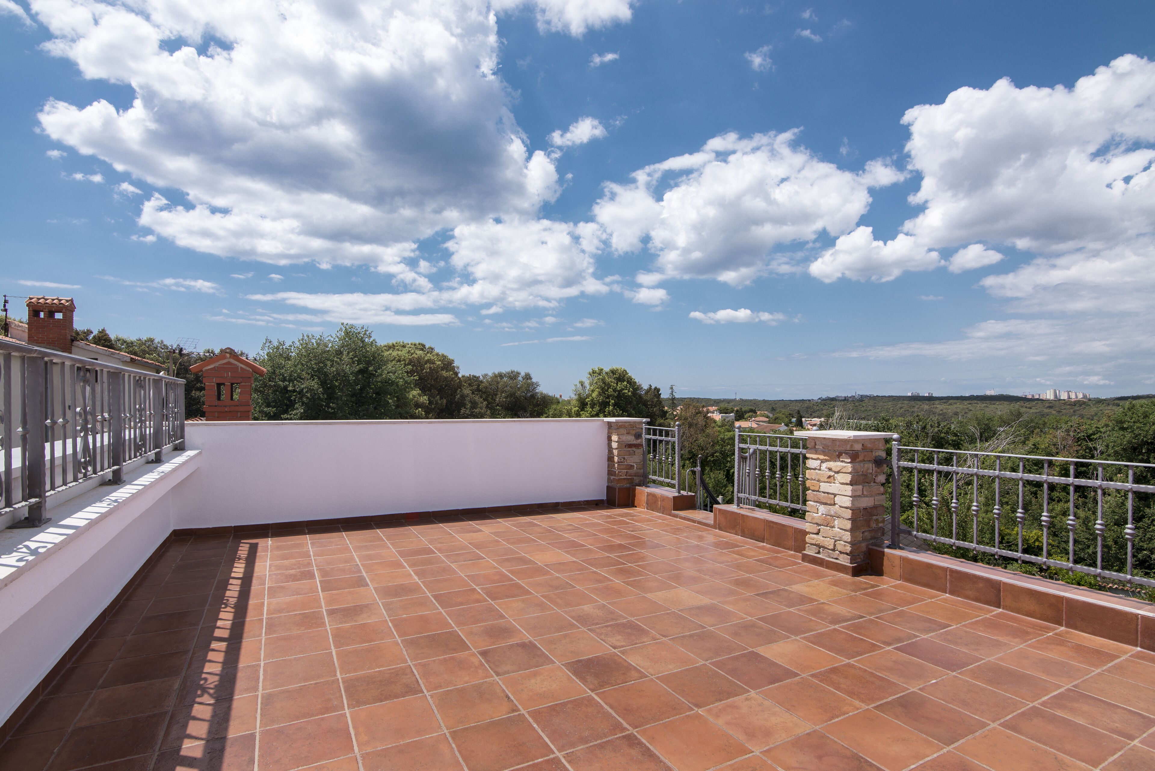 Une terrasse sur le toit, avec des carreaux de terre cuite, un mur blanc et une rambarde en métal.