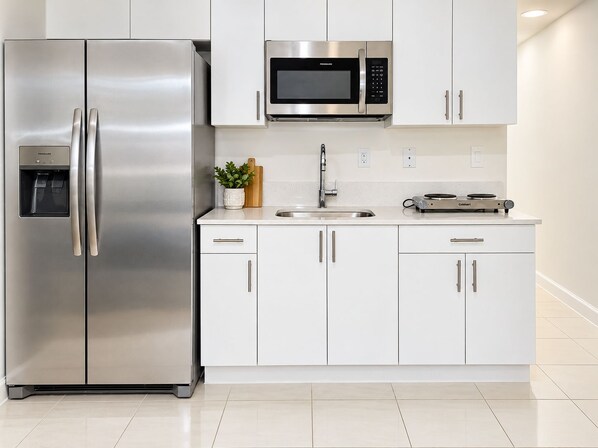 A modern kitchen with stainless steel appliances, white cabinetry, and a built-in microwave. - Private & Comfy Efficiency (Miami)
