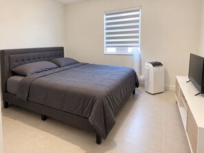 A bedroom with a bed, a TV, a heater, and a window with blinds. - Private & Comfy Efficiency (Miami)