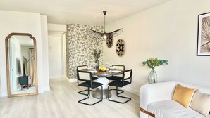 Ein modernes Wohnzimmer mit einem weißen Sofa, einem Esstisch mit Stühlen, einem Spiegel und einem Deckenventilator.