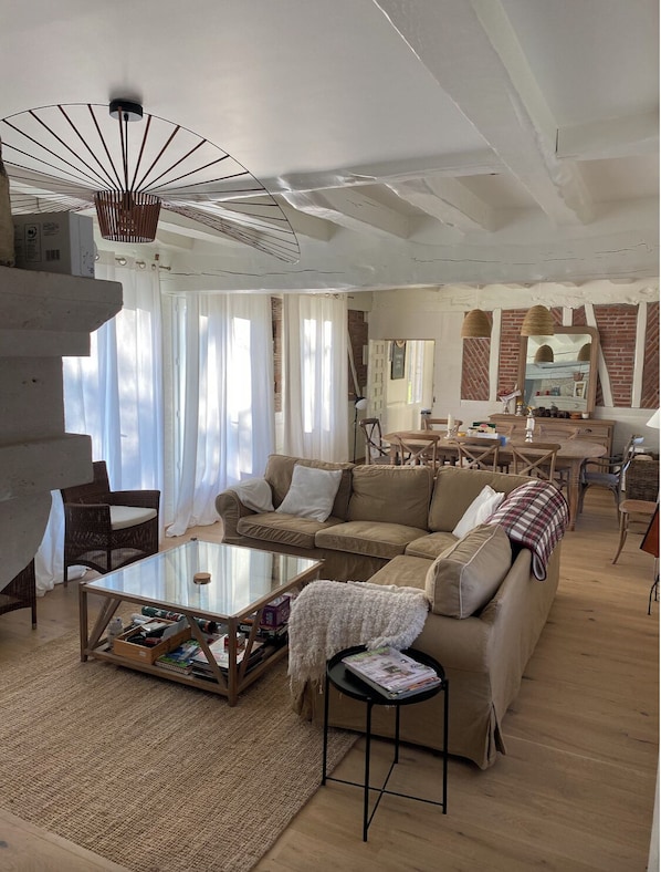 A spacious living room with a large sofa, a glass coffee table, and a dining area with a brick wall and wooden furniture.