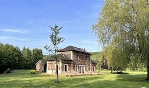 A large, two-story house with a stone facade and a sloped roof, surrounded by a well-maintained lawn and trees.