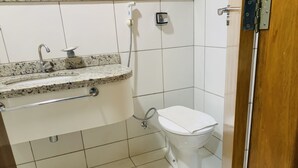 Une salle de bain avec des toilettes blanches, un lavabo doté d’un plan de travail en granit et une douchette à main.