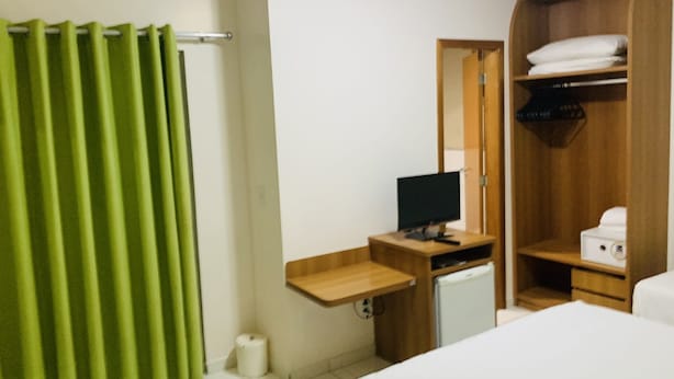 Une chambre d’hôtel comprenant un lit, un bureau avec un ordinateur, un petit réfrigérateur et une armoire.