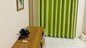 Une pièce avec une table en bois, un téléphone, un tableau encadré, un rideau vert et un appareil de climatisation.