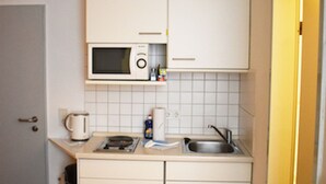 Eine kleine Küche mit weißen Schränken, einer Mikrowelle, einem Wasserkocher und einem Spülbecken.